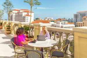 Two women sitting outside, working on their laptops, at a Quest Workspace center